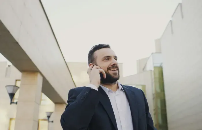 Smiling businessman in suit making a phone call outdoors between modern office buildings for Town Service Map